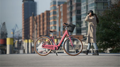 Eine Frau läuft in einer Stadt zu einem rosa Cube Ella Hybrid E-Bike.