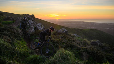 Zwei Radfahrer fahren einen Berg hinunter, jeweils auf einem Cube Stereo Fully Mountainbike.