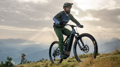 Zu sehen ist ein Mann auf einem grauen Cube Stereo Hybrid E-Bike, welcher auf einem Wanderweg unterwegs ist.