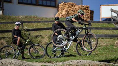 Ein Kind springt mit einem Cube Stereo Fully Mountainbike, zwei Radfahrer schauen zu.