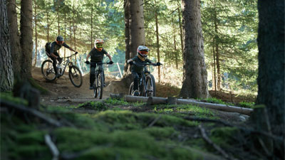 Zwei Jugendliche und ein Radfahrer fahren durch den Wald auf Cube Stereo Fully Mountainbikes.